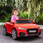 Mergaitė sėdi raudoname vaikiškame Audi automobilyje lauke