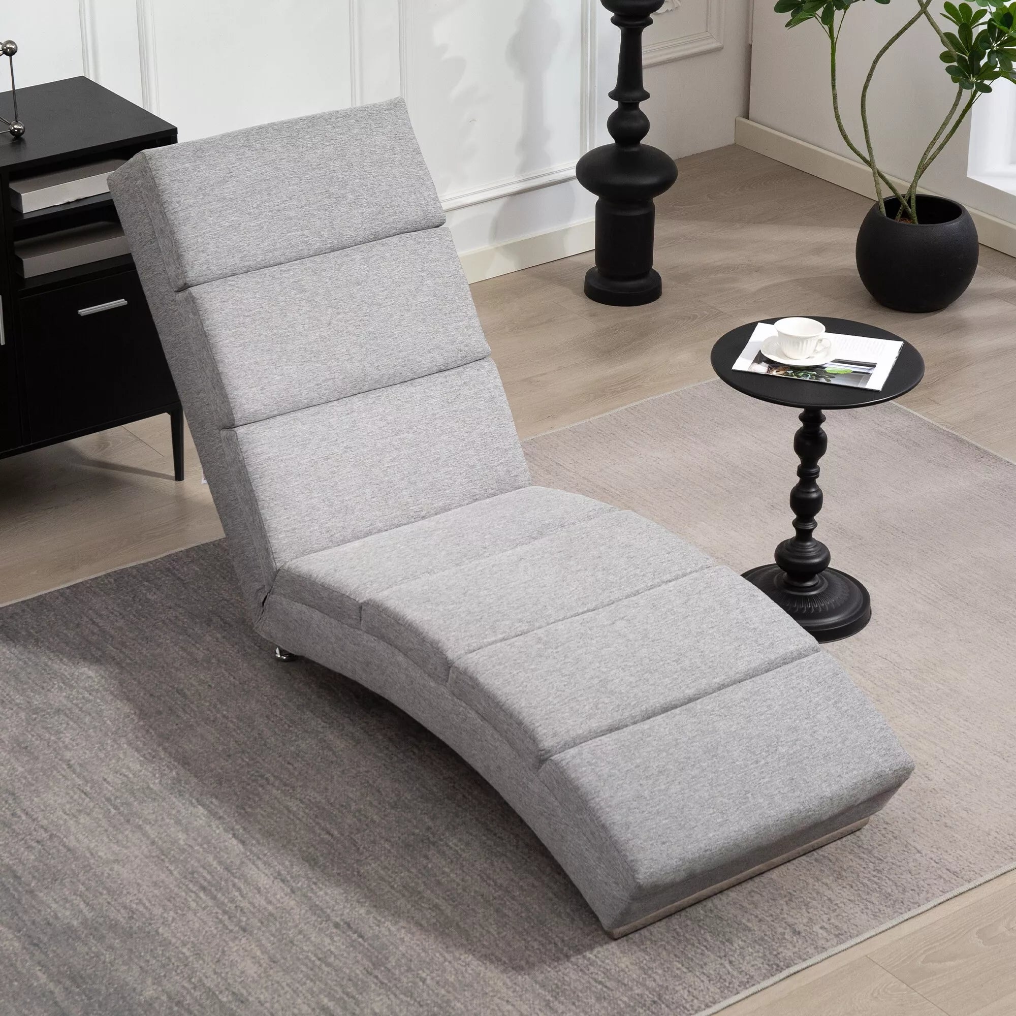 Pilkas chaiselongue fotelis iš šono, pavaizduotas grakštus S formos profilis