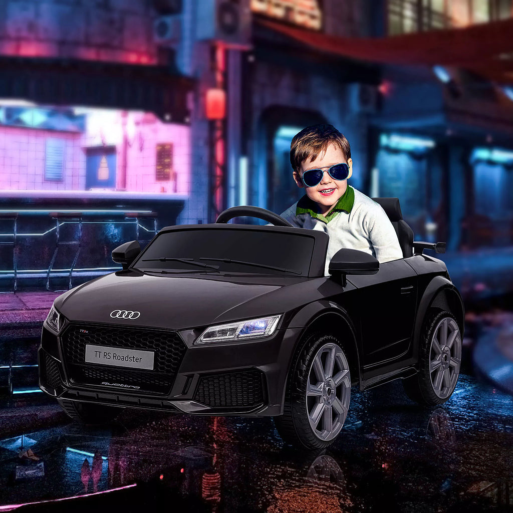 Berniukas sėdi juodame vaikiškame Audi automobilyje