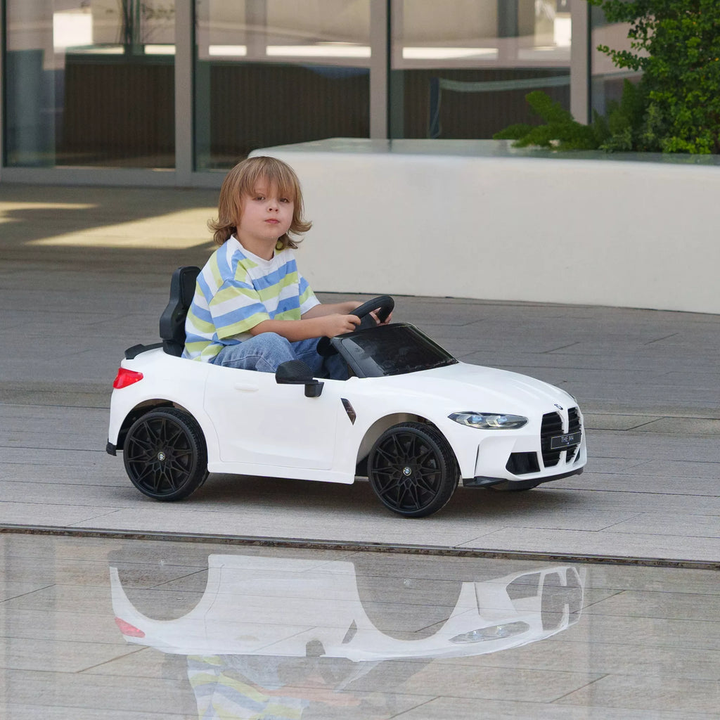 Vaikas važiuoja baltu elektriniu BMW M4 automobiliu
