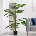 Dirbtinė monstera kambaryje prie pilkos sofos