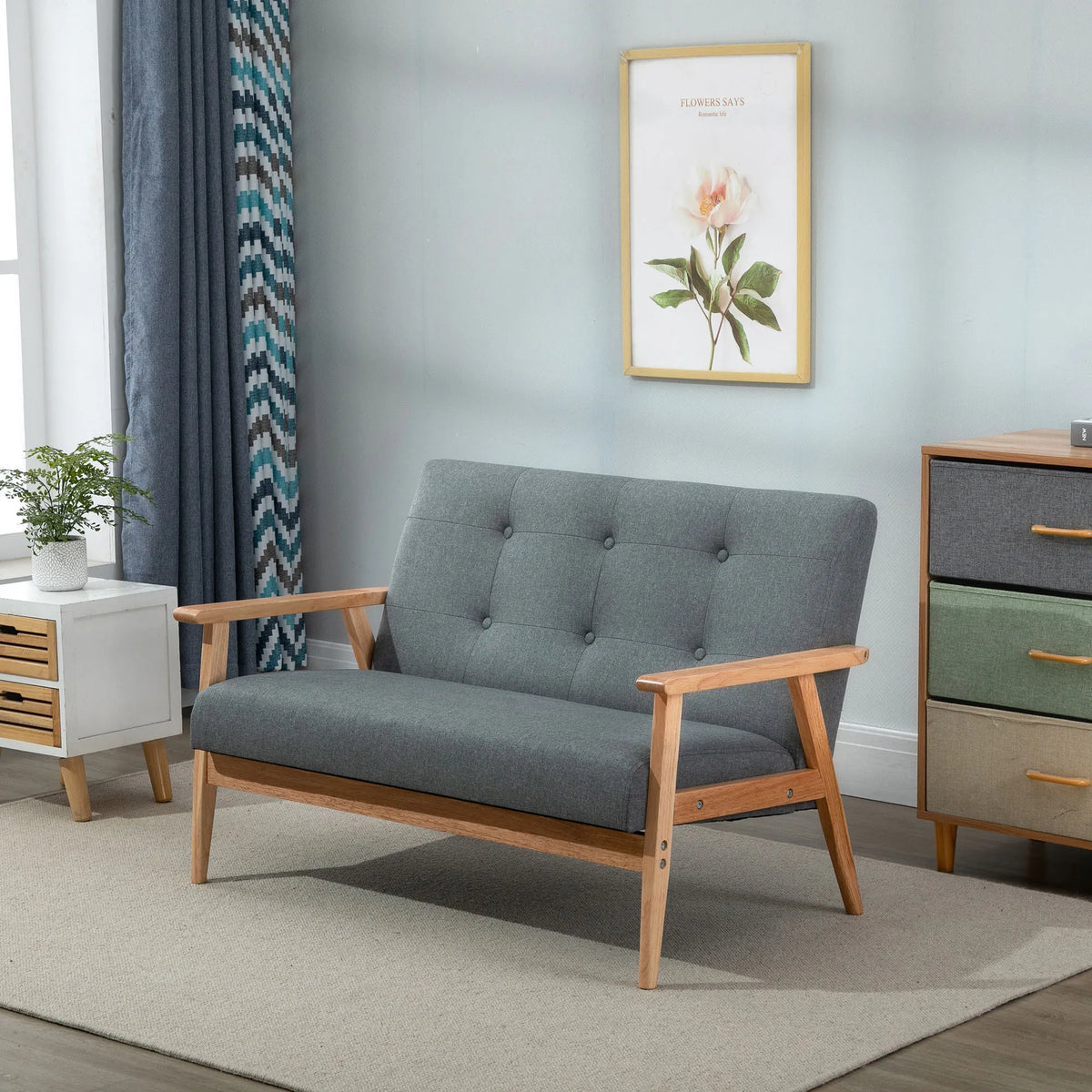 Pilka dvivietė sofa svetainėje tarp užuolaidos ir spintelės