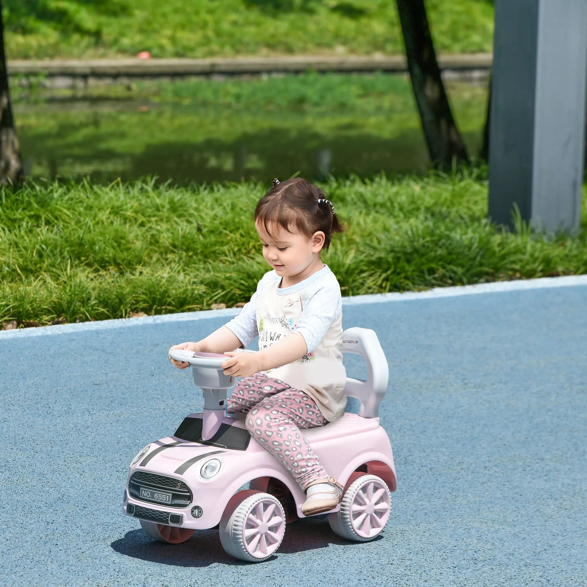 Mergaitė važiuoja rožiniu stumiamuoju automobiliu lauke