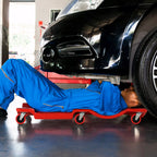 Mechanikas guli ant raudonos riedlentės po automobiliu