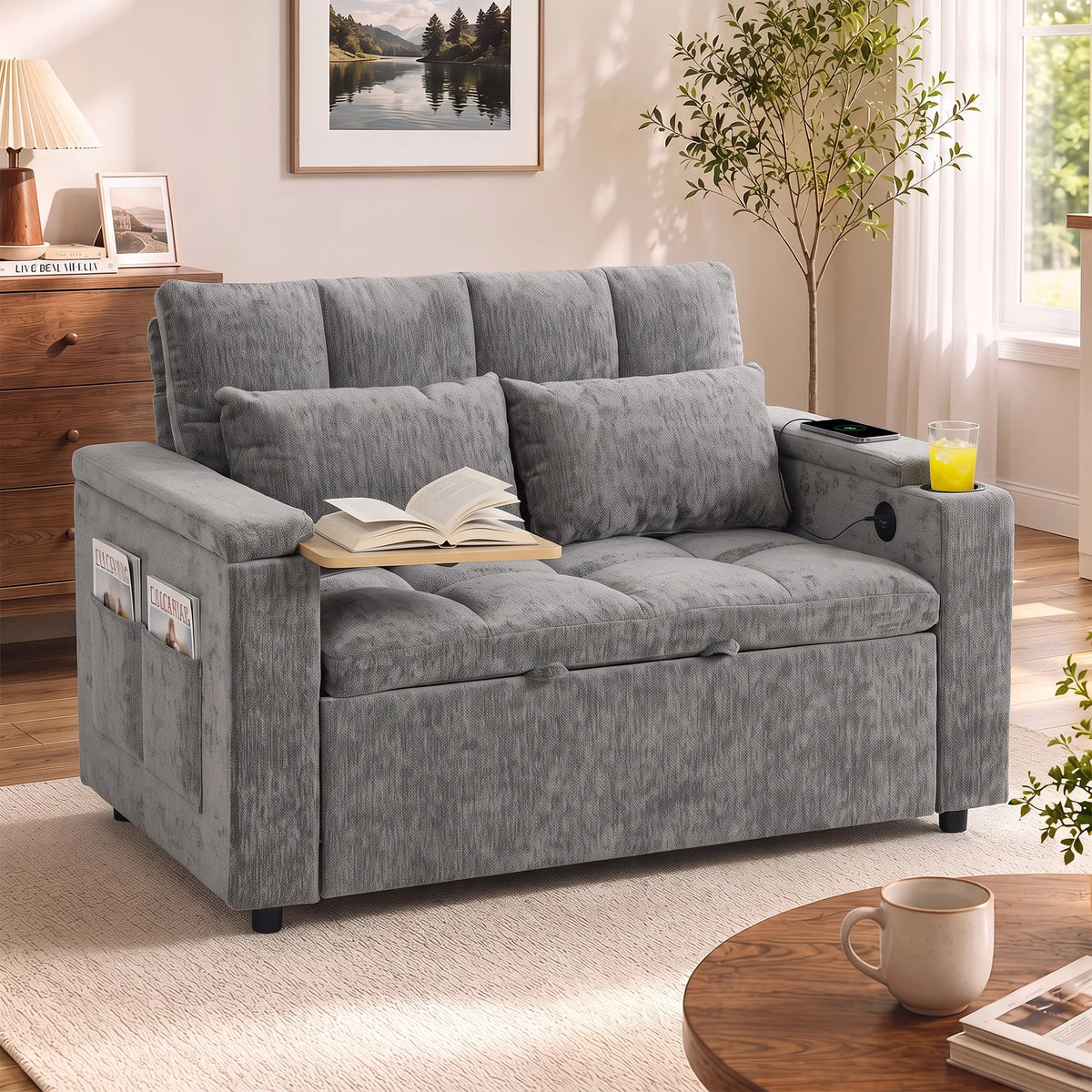 Pilka sofa su atversta knyga ant porankio ir apvaliu staliuku priekyje