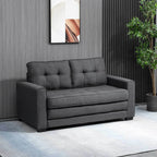Pilka sofa lova kambaryje šalia aukšto vazoninio augalo