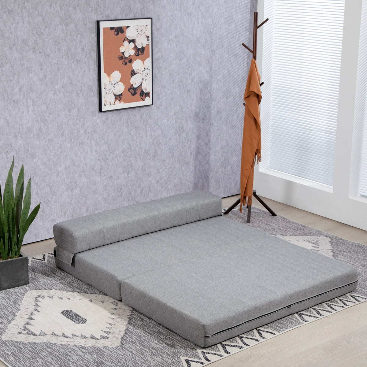 Pilka sofa-lova kambaryje šalia drabužių pakabos ir gėlių paveikslo
