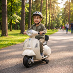Berniukas su šalmu važiuoja vaikišku elektriniu motociklu parke