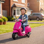 Kieme prie namo mergaitė su šalmu važiuoja Vespa motociklu