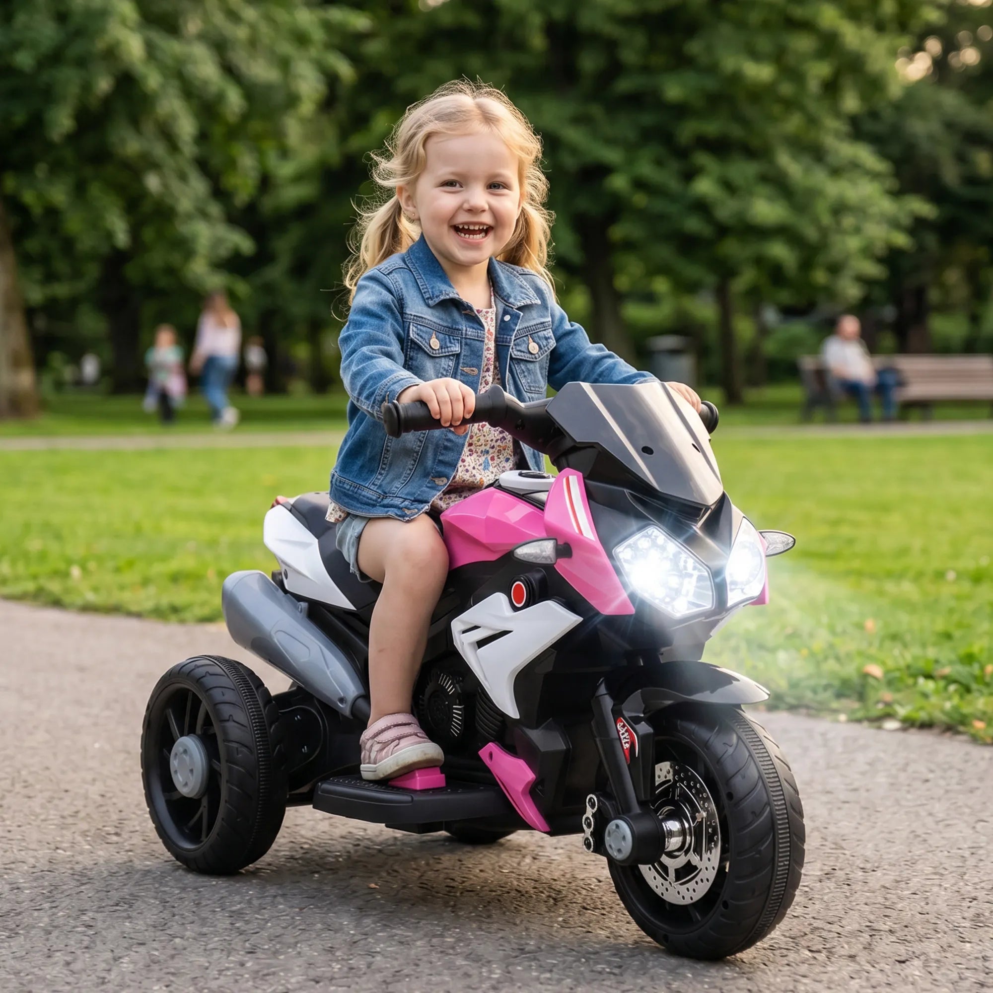 Mergaitė džiaugsmingai važiuoja elektromotociklu parko takeliu be šalmo