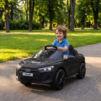 Berniukas vairuoja juodą vaikišką elektromobilį parko alėjoje