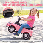 Sėdėdama ant rožinio automobiliuko mergaitė šypsosi lauke