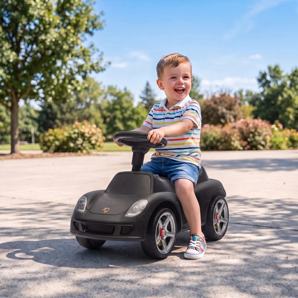 Berniukas linksmai važiuoja juodu stumduku-automobiliu šaligatviu
